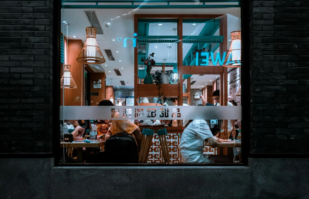 View of a cozy restaurant interior through a window, capturing a nighttime dining atmosphere.