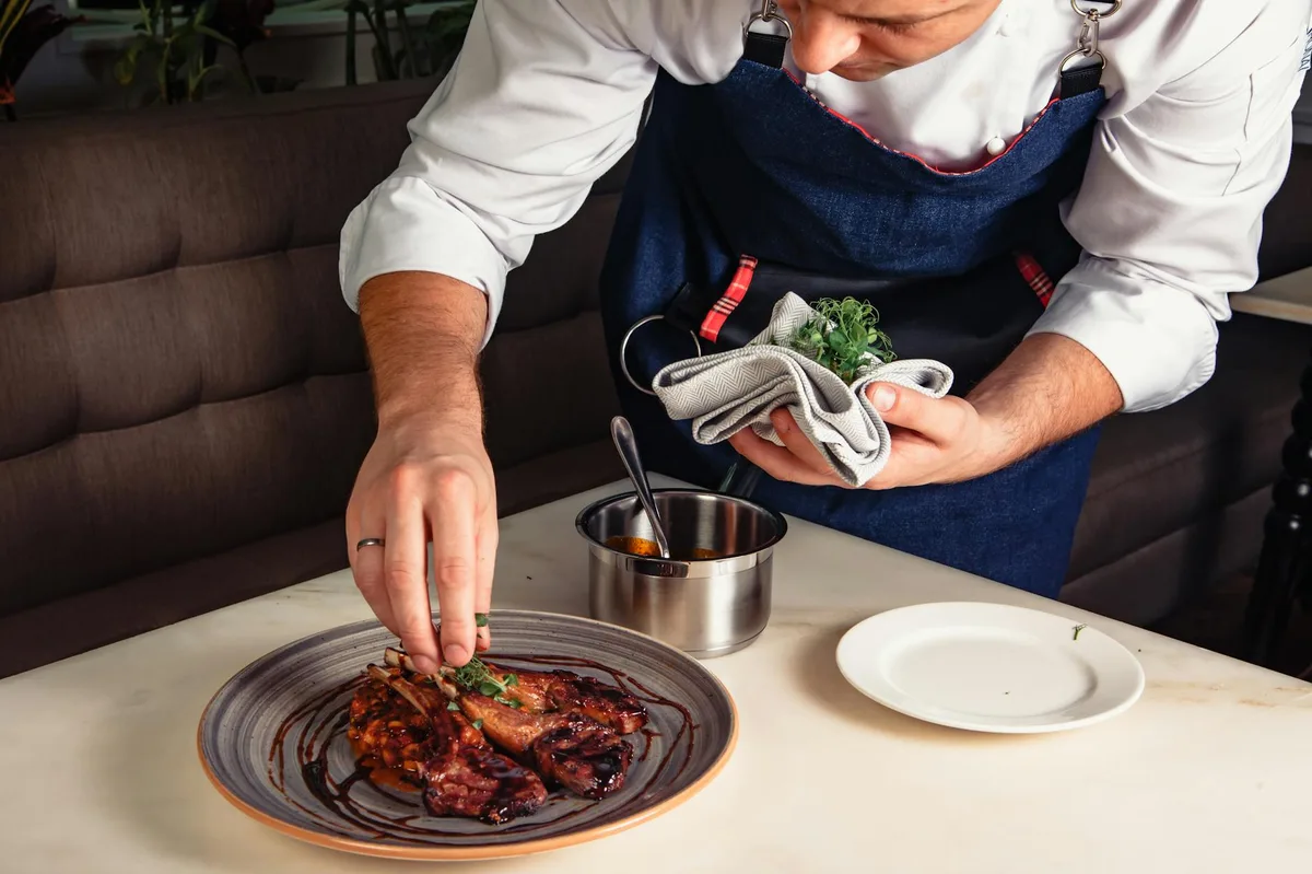 Close-up of a chef in Dubai plating a gourmet lamb dish in a restaurant.