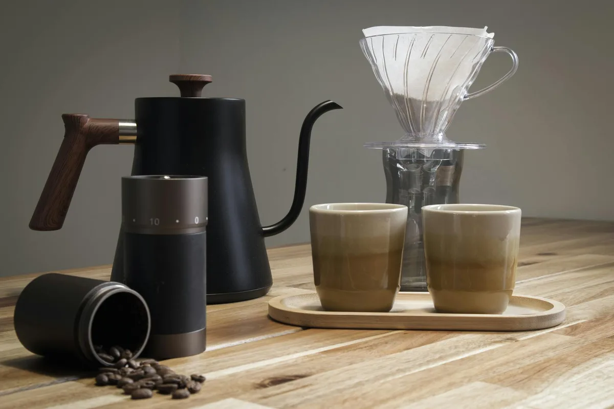 A stylish selection of coffee brewing tools including a V60 dripper, kettle, and grinder on a wooden table.